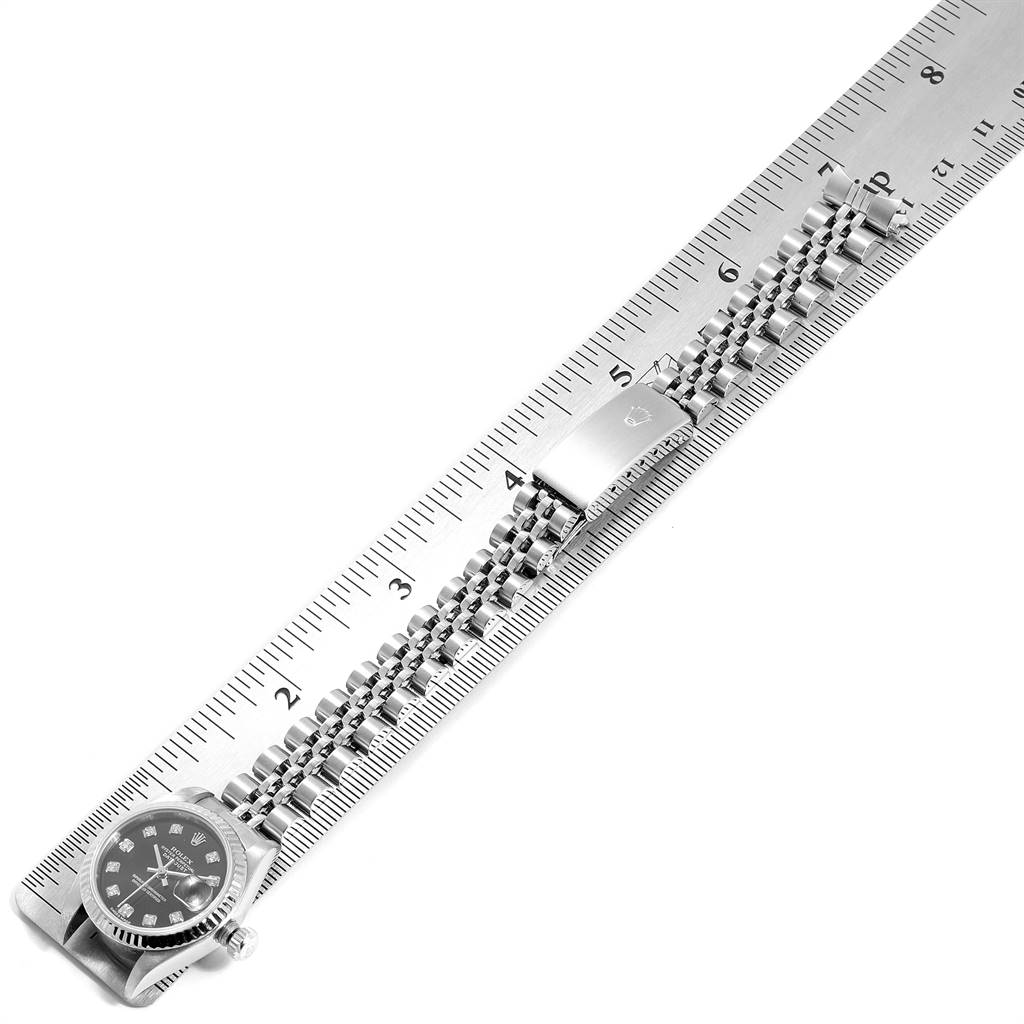 The Rolex Datejust 79174 Women
s Stainless Steel Black Dial 79174 Women
s Stainless Steel Black Dial watch is shown from a top-down angle with a focus on its bracelet and clasp, alongside a ruler for scale.