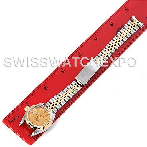 The Rolex Datejust 69173 Women's Stainless Steel Champagne Dial 69173 Women's Stainless Steel Champagne Dial watch is shown in a flat lay with its band fully extended alongside a red ruler.