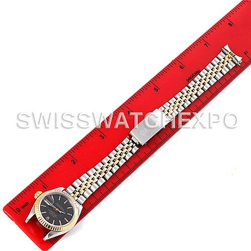 The Rolex Datejust 69173 Women's Stainless Steel Black Dial 69173 Women's Stainless Steel Black Dial watch is shown from a top-down angle with the entire band laid flat along a red ruler.