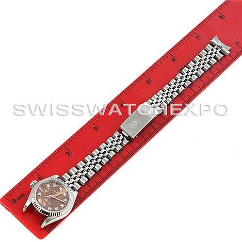 The image shows an overhead view of a Rolex Datejust 79174 Women's Stainless Steel Brown Dial 79174 Women's Stainless Steel Brown Dial watch with its full bracelet displayed on a red ruler for measurement.