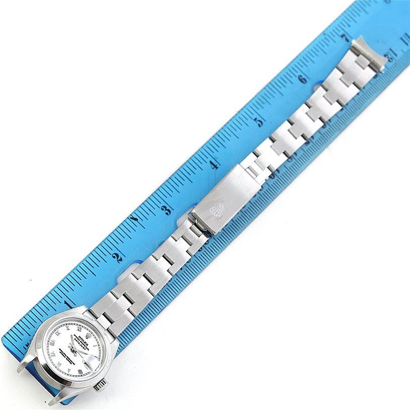 The Rolex Datejust 79160 Women
s Stainless Steel White Dial 79160 Women
s Stainless Steel White Dial watch is shown from a top-down angle, with its face and metal bracelet, against a blue ruler background.