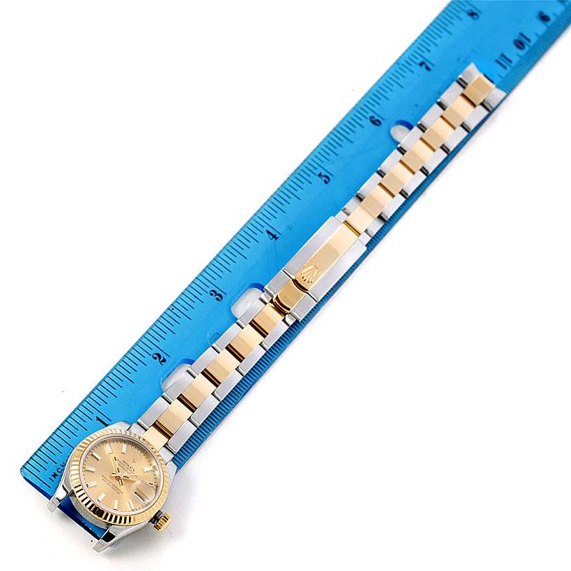 The Rolex Datejust 179173 Women's Steel and Gold (two tone) Champagne Dial 179173 Women's Steel and Gold (two tone) Champagne Dial watch is displayed flat with its band fully extended next to a blue ruler for measurement.