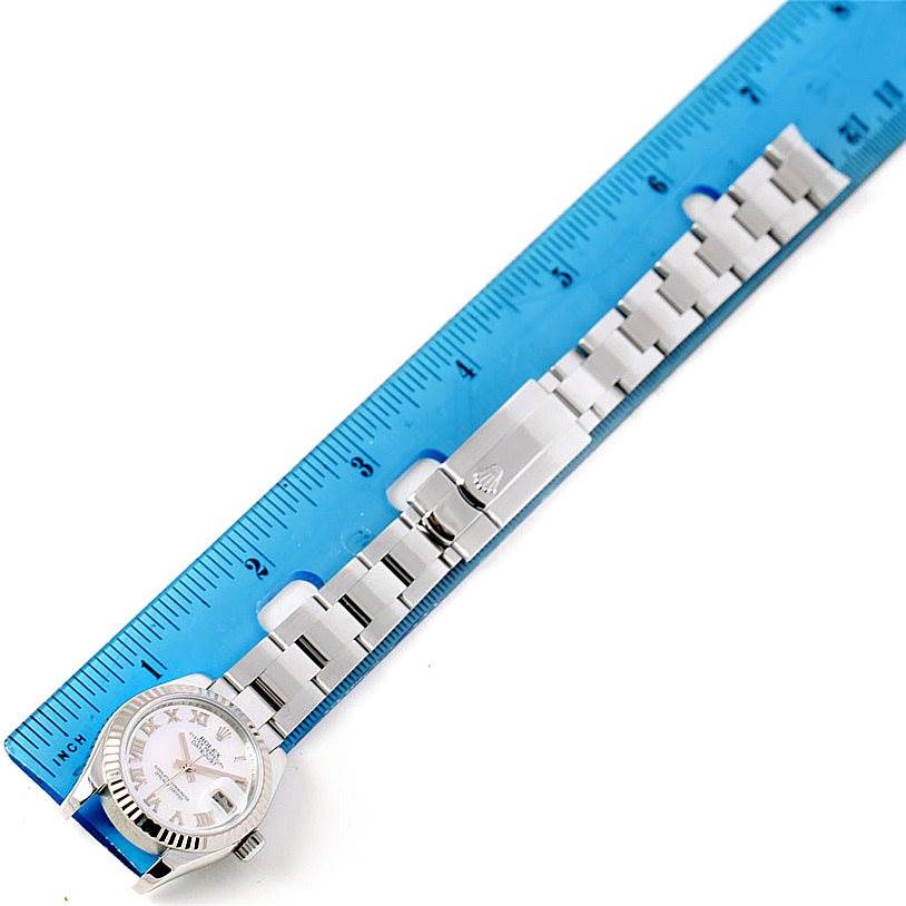 The Rolex Datejust 179174 Women's Stainless Steel Mother of Pearl Dial 179174 Women's Stainless Steel Mother of Pearl Dial watch is shown from an overhead angle, highlighting its bracelet and clasp next to a ruler.