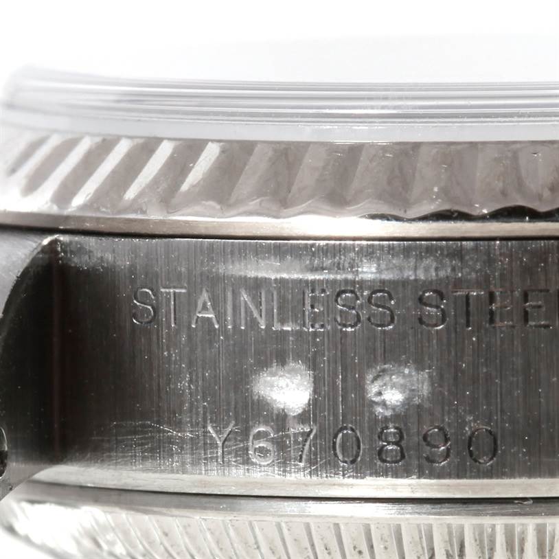 This close-up image shows the stainless steel side of a Rolex Datejust 79174 Women's Stainless Steel White Dial 79174 Women's Stainless Steel White Dial watch, including part of its fluted bezel and engraved serial number.