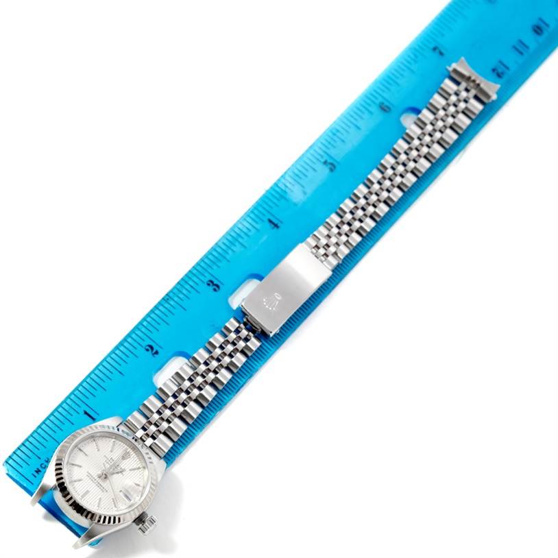 The Rolex Datejust 79174 Women's Stainless Steel Silver Dial 79174 Women's Stainless Steel Silver Dial watch is shown in a top-down view, displaying the face, bezel, and full Jubilee bracelet against a ruler.