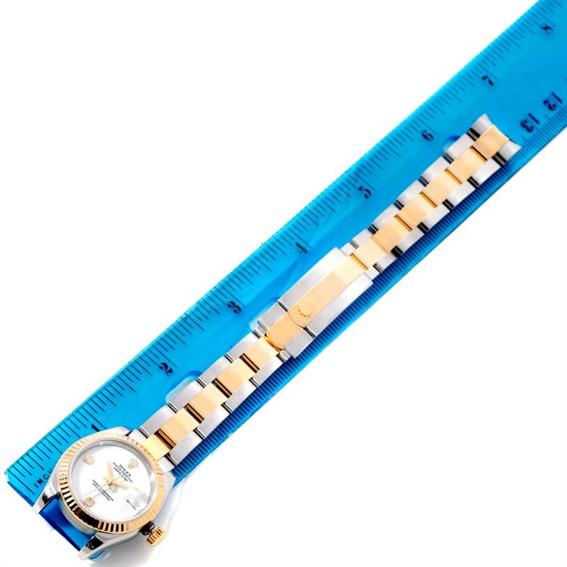 The photo shows a Rolex Datejust 179173 Women
s Steel and Gold (two tone) White Dial 179173 Women
s Steel and Gold (two tone) White Dial watch with a two-tone bracelet and clasp, aligned next to a blue ruler.