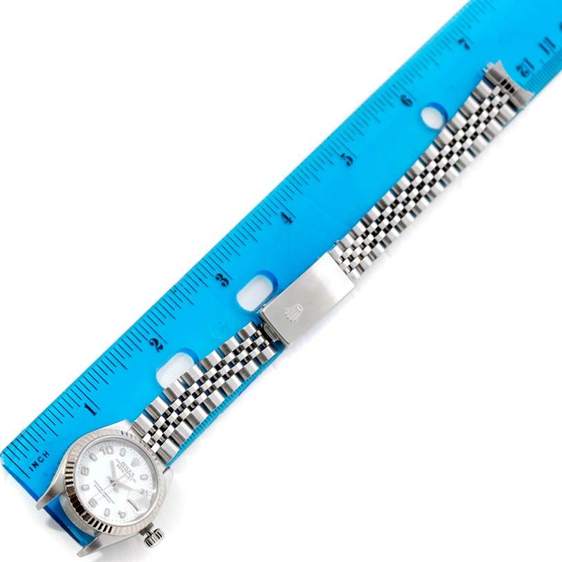 The Rolex Datejust 79174 Women
s Stainless Steel White Dial 79174 Women
s Stainless Steel White Dial watch is shown from a top view, displaying the face, bezel, and bracelet next to a blue ruler.