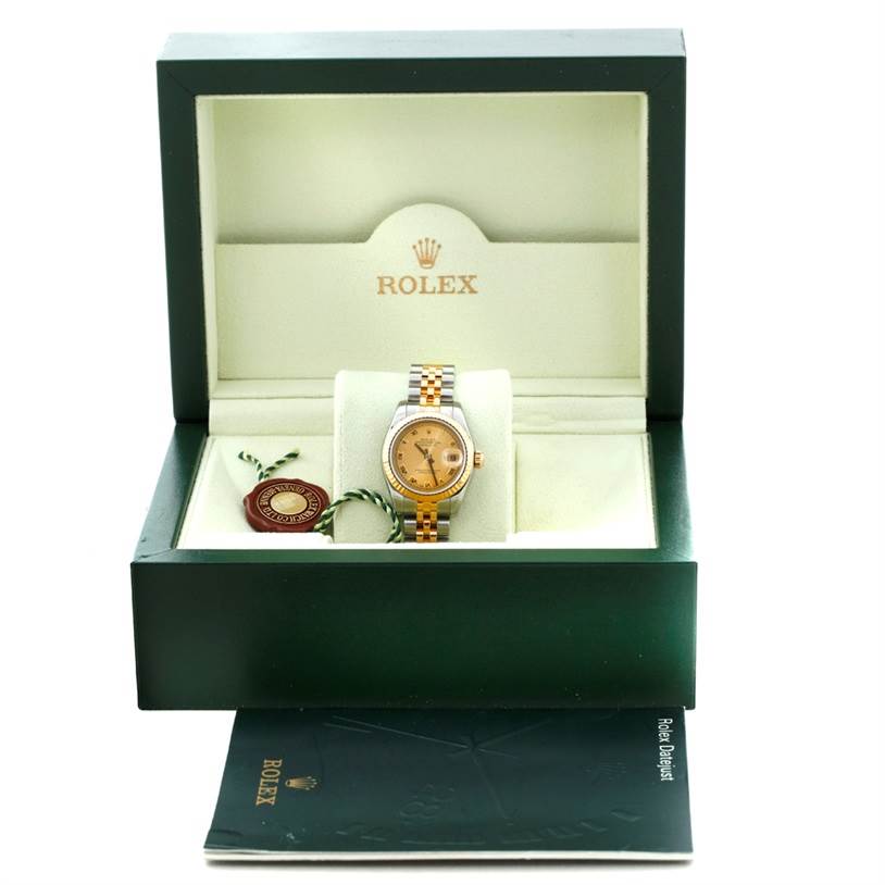 This image shows a Rolex Datejust 179173 Women's Steel and Gold (two tone) Champagne Dial 179173 Women's Steel and Gold (two tone) Champagne Dial watch in its open, green presentation box, along with a tag and documents placed in front.