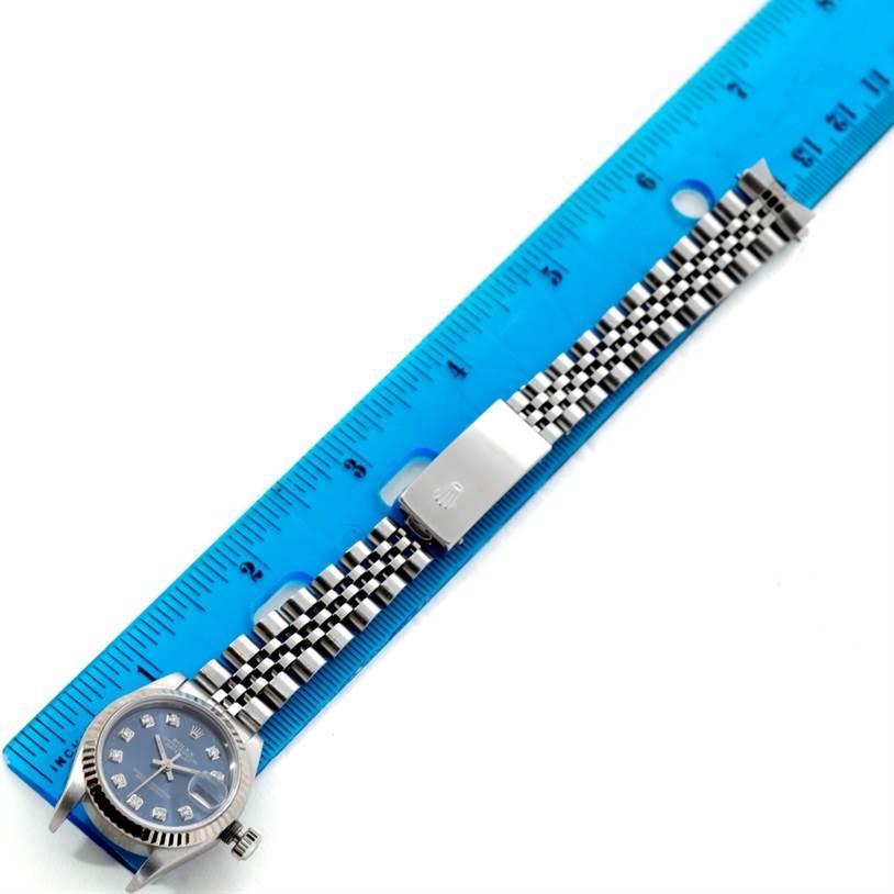 The Rolex Datejust 79174 Women's Stainless Steel Blue Dial 79174 Women's Stainless Steel Blue Dial watch is shown at an overhead angle, displaying its face, band, and clasp next to a blue ruler.