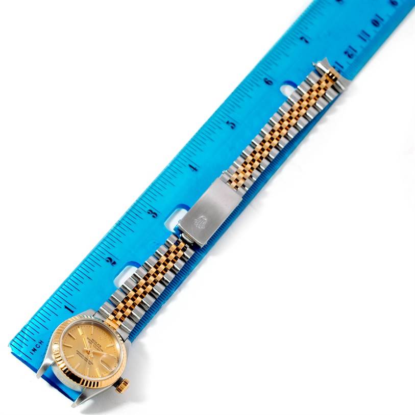 The image shows a Rolex Datejust 79173 Women's Stainless Steel Champagne Dial 79173 Women's Stainless Steel Champagne Dial watch placed horizontally next to a blue ruler, highlighting the gold dial and metal bracelet.