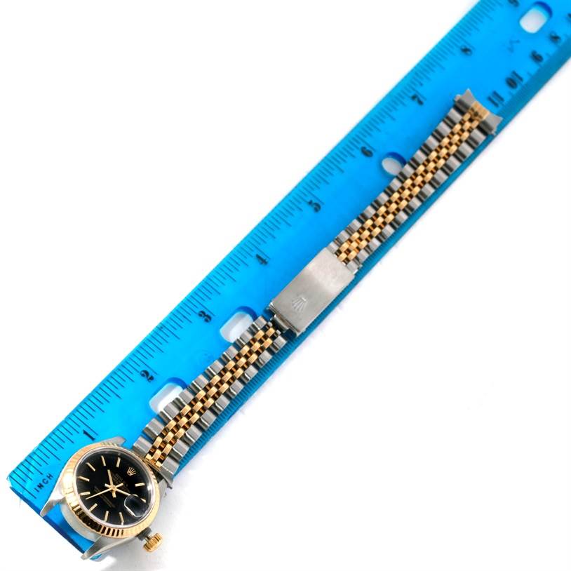 The image shows the face, crown, and two-tone bracelet of a Rolex Datejust 69173 Women
s Stainless Steel Black Dial 69173 Women
s Stainless Steel Black Dial watch alongside a blue ruler.