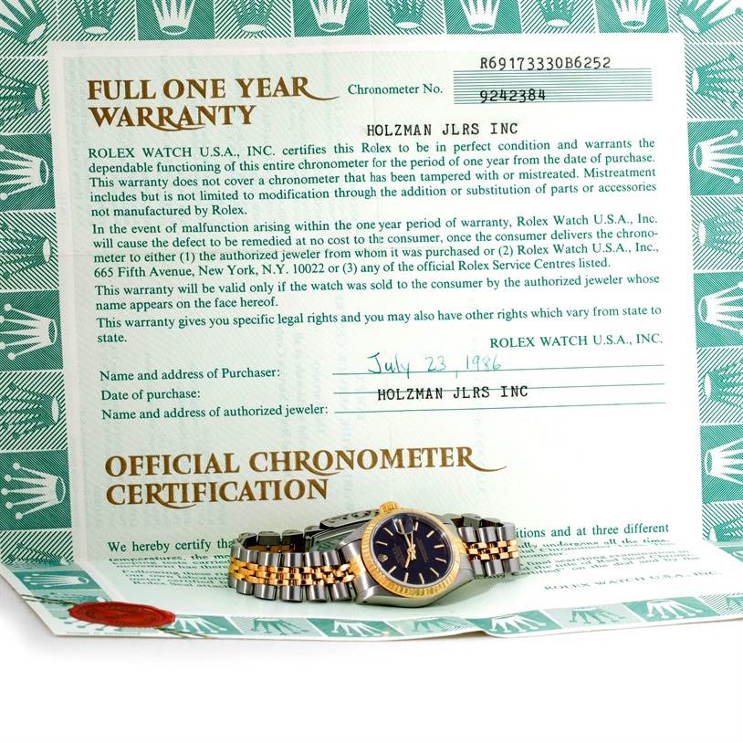 The Rolex Datejust 69173 Women
s Stainless Steel Black Dial 69173 Women
s Stainless Steel Black Dial watch is displayed horizontally in front of its warranty and certification papers.