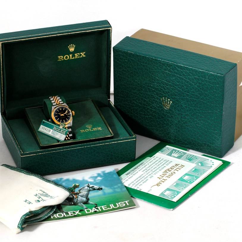 The image shows a Rolex Datejust 69173 Women
s Stainless Steel Black Dial 69173 Women
s Stainless Steel Black Dial watch at an angled front view inside its box, with additional packaging and documents around it.