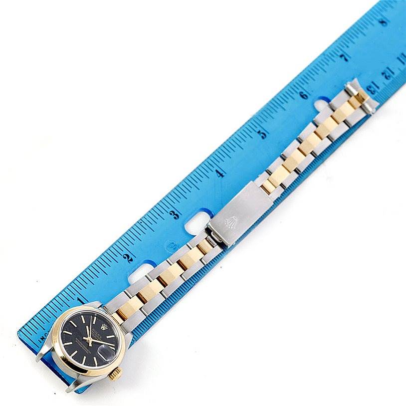 The image shows a Rolex Datejust 79163 Women's Steel and Gold (two tone) Black Dial 79163 Women's Steel and Gold (two tone) Black Dial watch placed alongside a blue ruler for measurement, displaying its face, bezel, bracelet, and clasp.