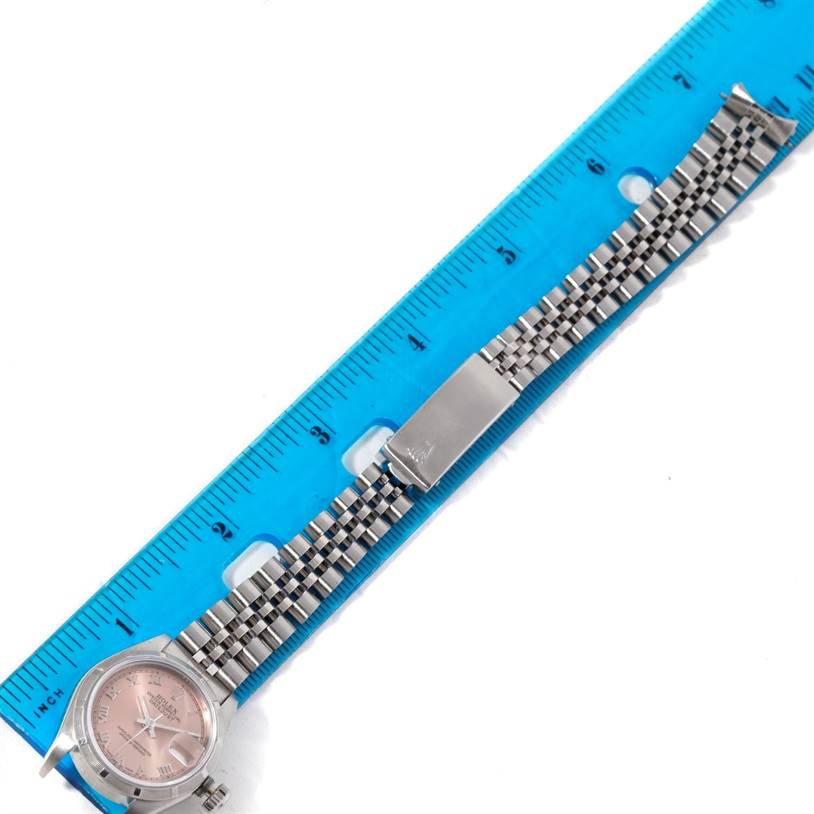 The Rolex Datejust 69190 Women's Stainless Steel Pink Dial 69190 Women's Stainless Steel Pink Dial watch is shown from a top-down angle, displaying the face, strap, and clasp next to a blue ruler for scale.