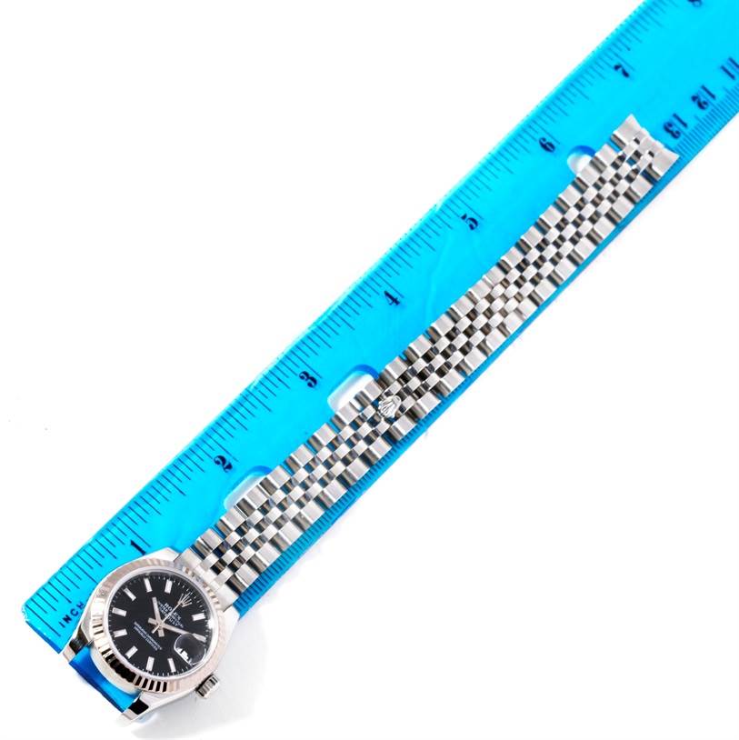 The image shows a Rolex Datejust 179174 Women
s Stainless Steel Black Dial 179174 Women
s Stainless Steel Black Dial watch positioned next to a blue ruler to measure the length of its metal bracelet.