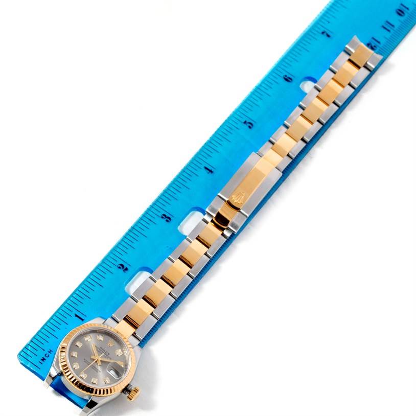 This image shows a Rolex Datejust 179173 Women's Steel and Gold (two tone) Grey Dial 179173 Women's Steel and Gold (two tone) Grey Dial watch with a gold and stainless steel bracelet laid next to a blue ruler.