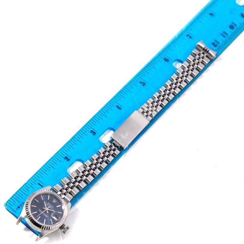 The Rolex Datejust 79174 Women's Stainless Steel Blue Dial 79174 Women's Stainless Steel Blue Dial watch is shown flat with the face and bracelet extended along a blue ruler for measurement.