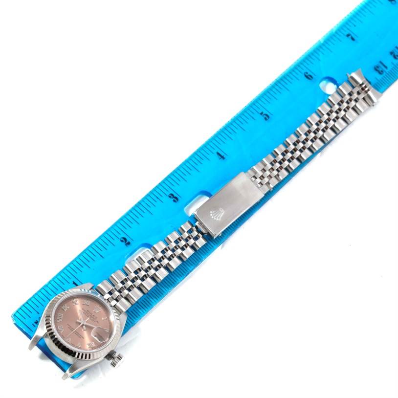 The image shows a Rolex Datejust 79174 Women's Stainless Steel Pink Dial 79174 Women's Stainless Steel Pink Dial watch's face and jubilee bracelet next to a blue ruler for scale.