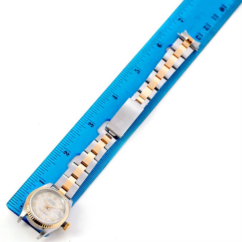 The Rolex Datejust 69173 Women's Stainless Steel Beige Dial 69173 Women's Stainless Steel Beige Dial watch is shown from above, displaying its face, gold bezel, two-tone bracelet, and clasp alongside a blue ruler.