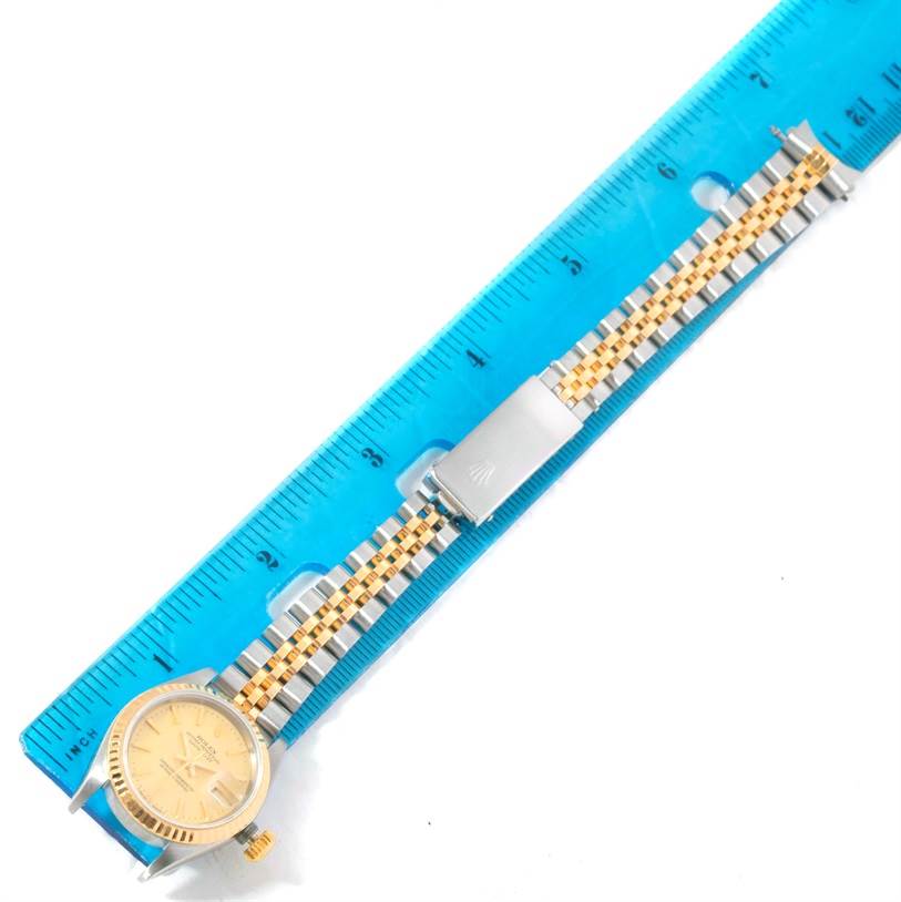 The image shows a top view of a Rolex Datejust 69173 Women
s Stainless Steel Champagne Dial 69173 Women
s Stainless Steel Champagne Dial watch next to a blue measuring ruler, highlighting its band and dial.