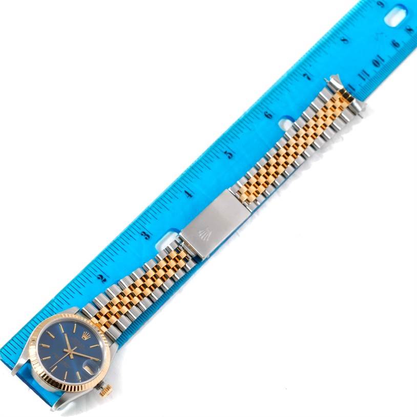 This image shows a top view of a Rolex Mid-Size 68273 Women's Steel and Gold (two tone) Blue Dial 68273 Women's Steel and Gold (two tone) Blue Dial watch, featuring its face, full bracelet, and clasp placed next to a blue ruler.