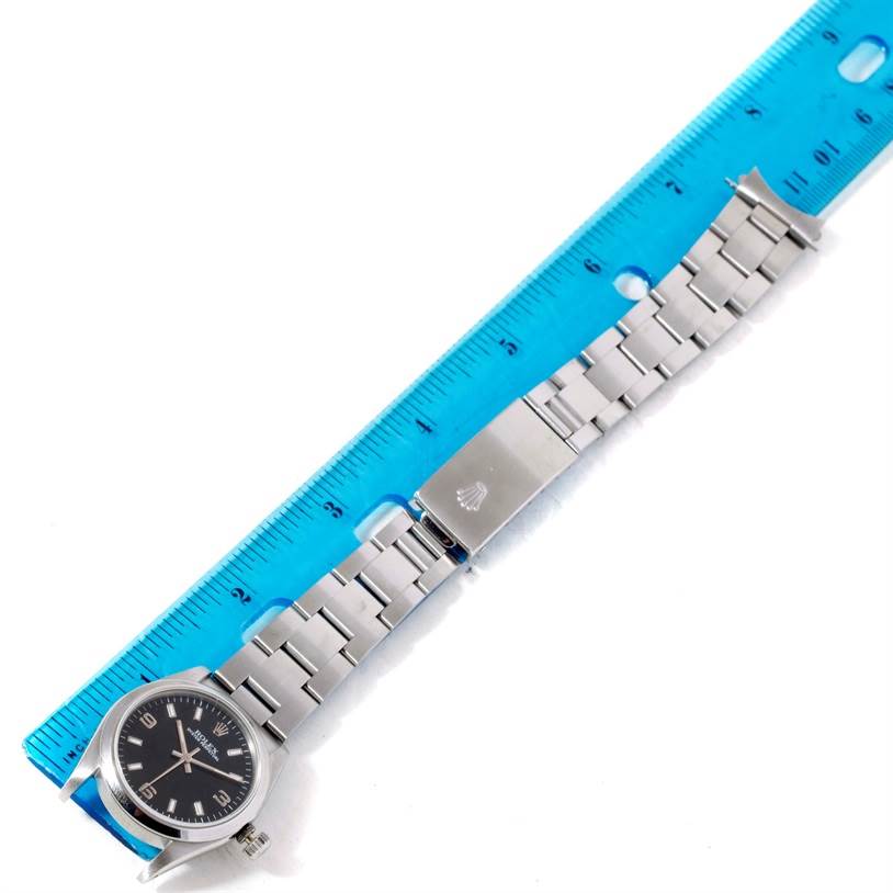 The image shows a Mid-Size Rolex watch with a black dial and stainless steel bracelet, partially measured against a blue ruler.