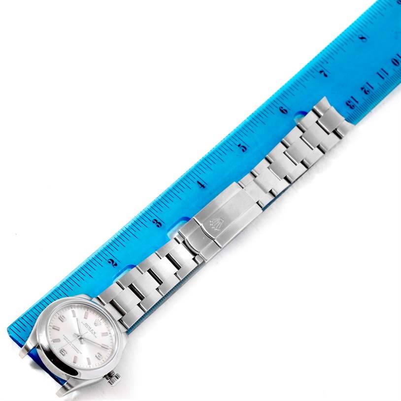 The Mid-Size Rolex watch is shown from an overhead angle, featuring the face, clasp, and part of the bracelet against a ruler.