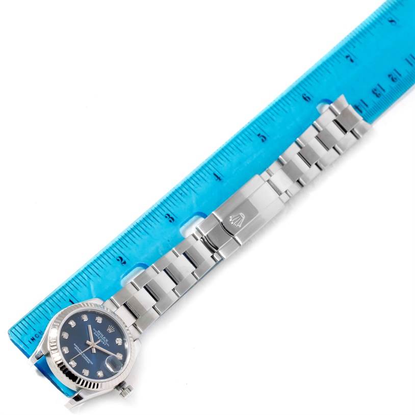 This image shows a top view of a Rolex Mid-Size 178274 Women's Stainless Steel Blue Dial 178274 Women's Stainless Steel Blue Dial watch with a blue face and metal bracelet, alongside a ruler.