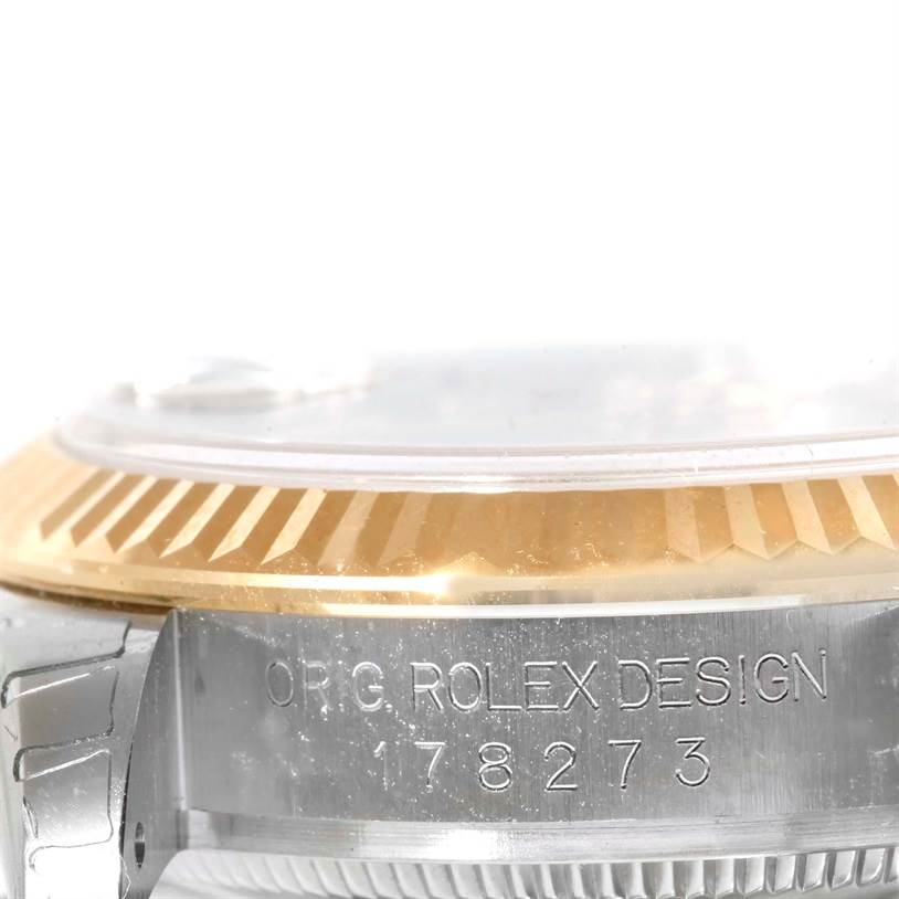 The image shows a close-up side angle of a Mid-Size Rolex watch, highlighting the bezel, part of the case, and the serial number engraving.