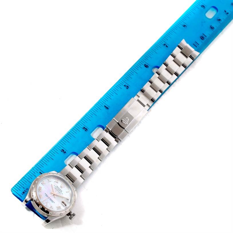 The Rolex Mid-Size 178344 Women's Stainless Steel Mother of Pearl Dial 178344 Women's Stainless Steel Mother of Pearl Dial model watch is shown lying flat, with its face, bracelet, and clasp visible, next to a blue ruler.