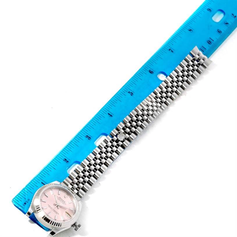 The image shows the Rolex Mid-Size 178274 Women's Stainless Steel Pink Dial 178274 Women's Stainless Steel Pink Dial watch laid flat along a blue ruler, displaying its pink dial and metal bracelet.