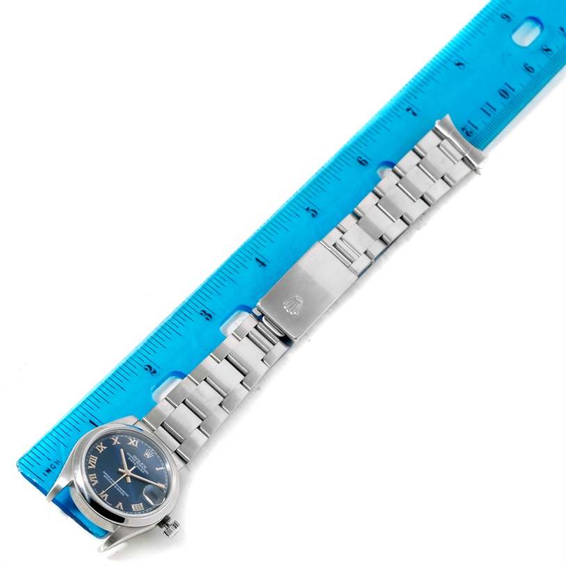 The image shows a Mid-Size Rolex watch placed next to a ruler, highlighting the watch face and metal bracelet from an overhead angle.