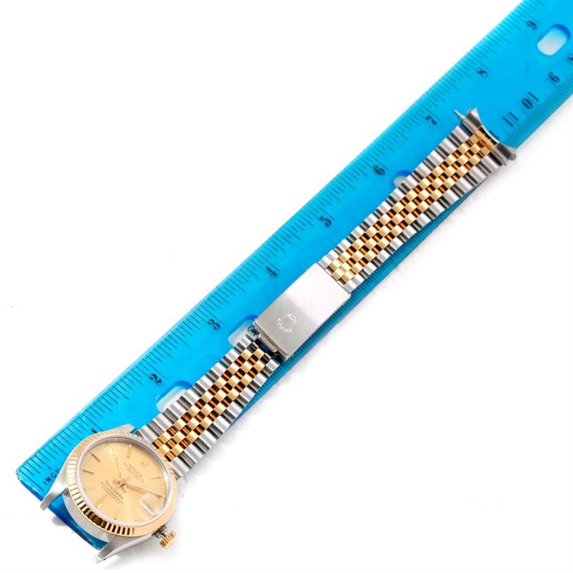 The Rolex Mid-Size 68273 Women's Steel and Gold (two tone) Champagne Dial 68273 Women's Steel and Gold (two tone) Champagne Dial watch is shown flat along a blue measuring ruler, showcasing its face and two-tone metal bracelet.