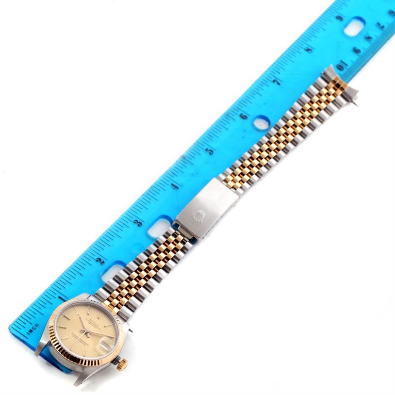 The mid-size Rolex watch is viewed from above, showing the face, bezel, and Jubilee bracelet alongside a blue ruler.
