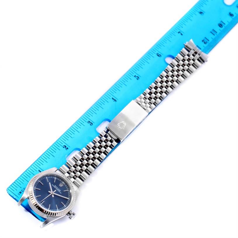 The image shows a Rolex Mid-Size 77014 Women's Stainless Steel Blue Dial 77014 Women's Stainless Steel Blue Dial model watch laid flat next to a blue ruler, displaying its face, jubilee bracelet, and clasp.