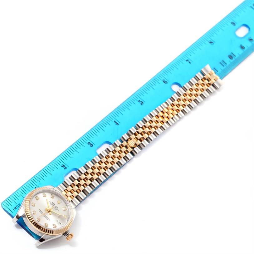 The Rolex Mid-Size 178273 Women's Steel and Gold (two tone) Silver Dial 178273 Women's Steel and Gold (two tone) Silver Dial watch is shown at a top-down angle with a blue ruler alongside, highlighting its bracelet and face.