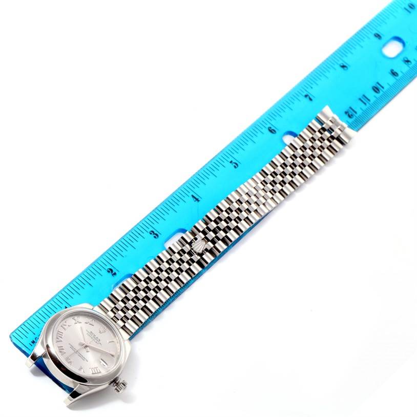 The image shows a Mid-Size Rolex watch facing up beside a blue ruler, highlighting its band and face.
