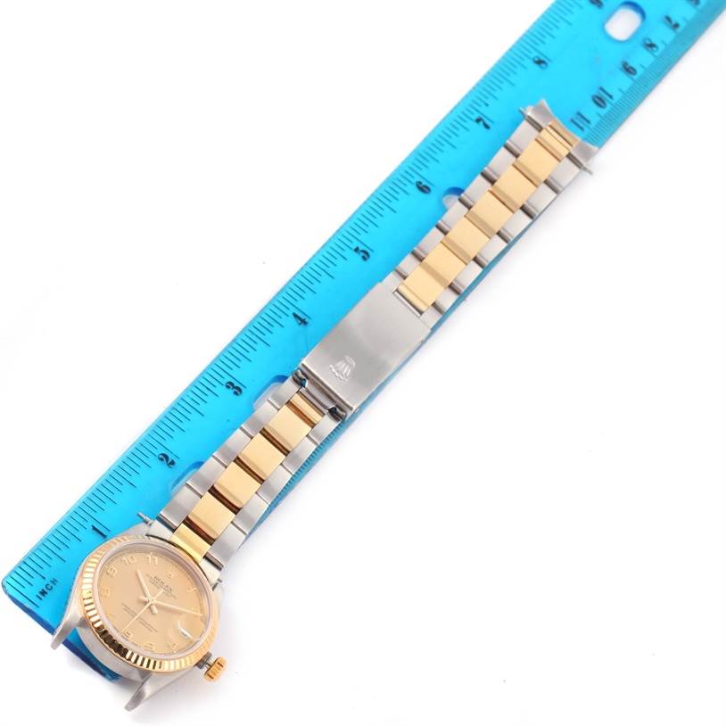 This image shows a Rolex Mid-Size 68273 Women's Steel and Gold (two tone) Champagne Dial 68273 Women's Steel and Gold (two tone) Champagne Dial watch laid flat with a gold and silver bracelet alongside a blue ruler.
