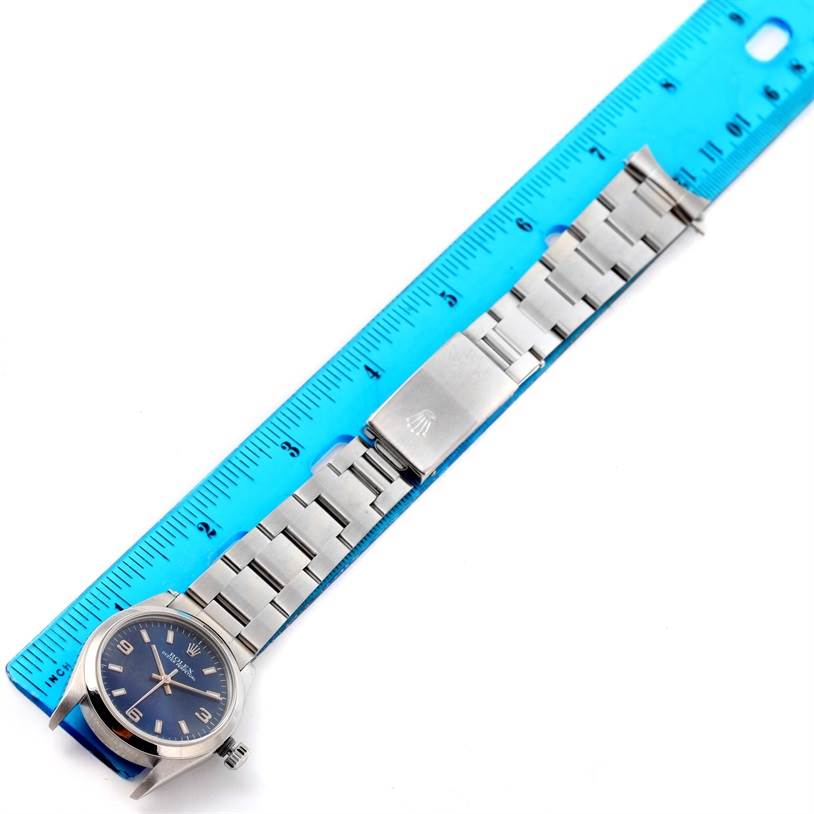 The image shows a Rolex Mid-Size 77080 Women's Stainless Steel Blue Dial 77080 Women's Stainless Steel Blue Dial watch laid flat alongside a blue ruler, highlighting its face, bracelet, and clasp.