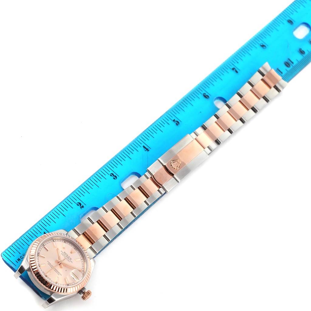 The image shows a Mid-Size Rolex watch laid flat next to a ruler, displaying the dial, bezel, crown, and full bracelet.