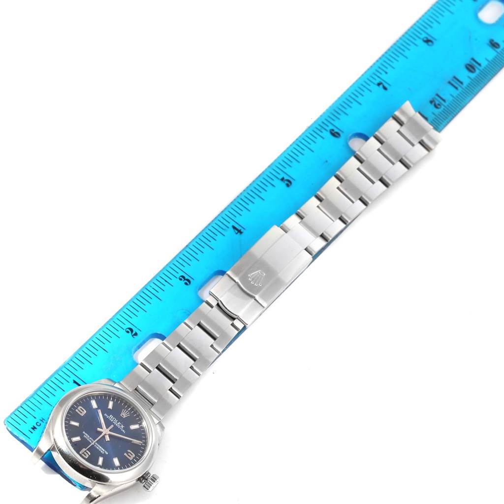 The image shows a Rolex Mid-Size 177200 Women's Stainless Steel Blue Dial 177200 Women's Stainless Steel Blue Dial watch laid flat next to a blue ruler, displaying its face and bracelet.