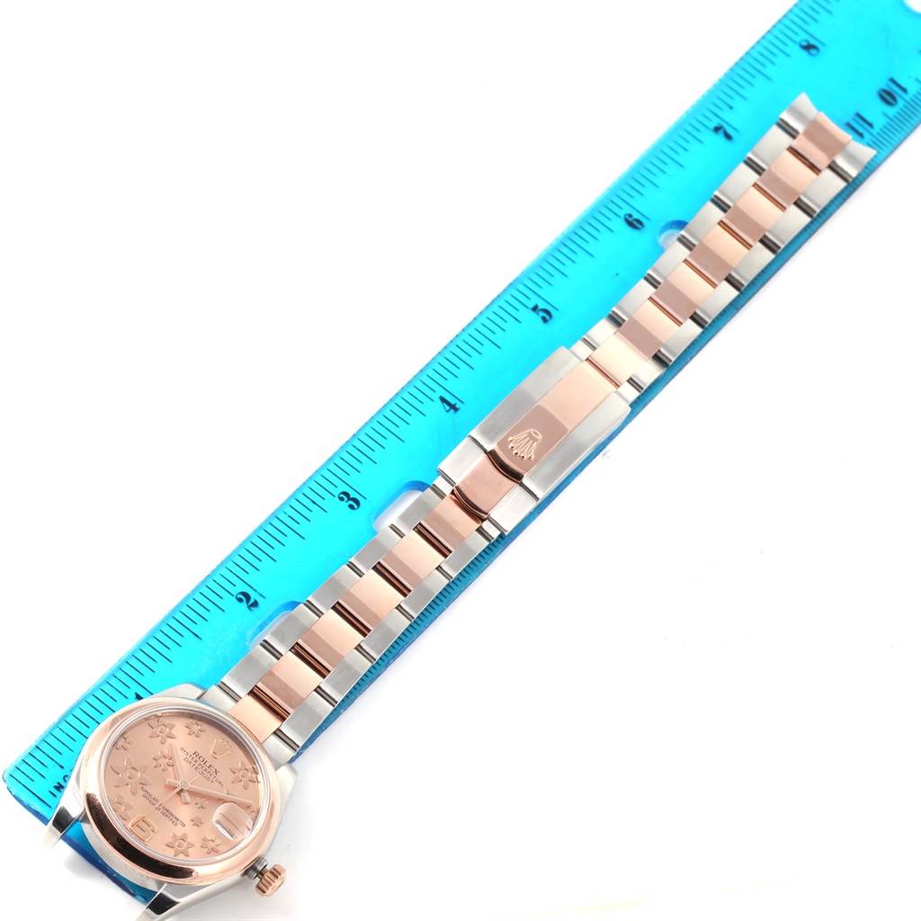 The image shows a Rolex Mid-Size 178241 Women's Steel and Gold (two tone) Pink Dial 178241 Women's Steel and Gold (two tone) Pink Dial watch laid flat alongside a blue ruler, highlighting the face, band, and clasp.