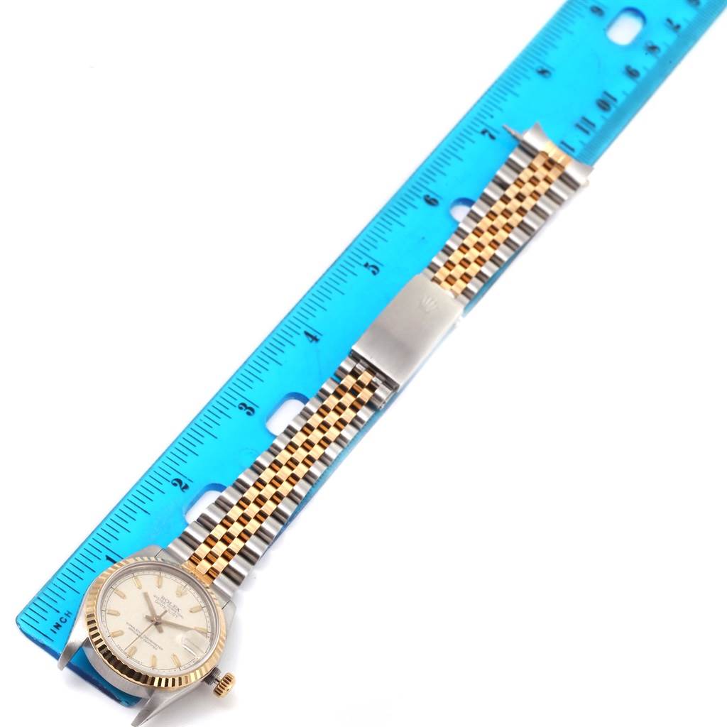 The image shows a top-down view of a Rolex Mid-Size 68273 Women's Steel and Gold (two tone) Beige Dial 68273 Women's Steel and Gold (two tone) Beige Dial watch, featuring its dial, bezel, crown, and bracelet laid along a ruler.