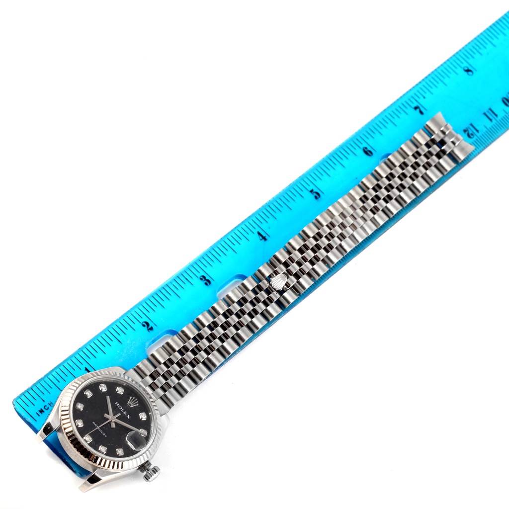 The Rolex Mid-Size 178274 Women's Stainless Steel Black Dial 178274 Women's Stainless Steel Black Dial watch is shown with its front dial and bracelet aligned next to a blue ruler.