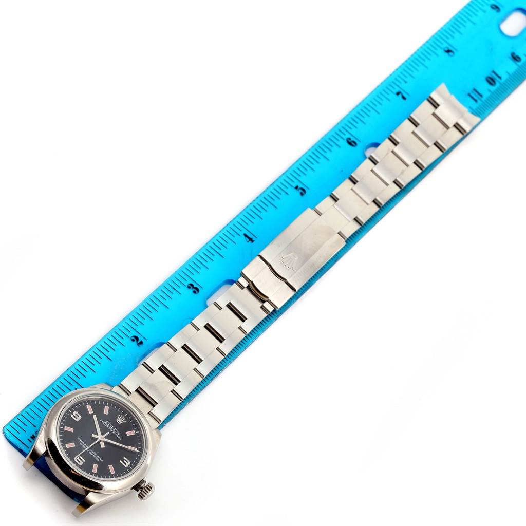 The Rolex Mid-Size 177200 Women's Stainless Steel Black Dial 177200 Women's Stainless Steel Black Dial model watch is positioned flat with its face, bezel, and stainless steel bracelet aligned next to a blue ruler.