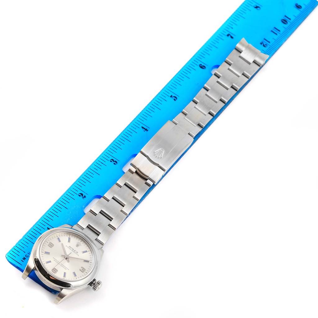 The image shows a top-down view of a Rolex Mid-Size 177200 Women's Stainless Steel Silver Dial 177200 Women's Stainless Steel Silver Dial watch displaying its face, bracelet, and clasp, placed next to a blue ruler.