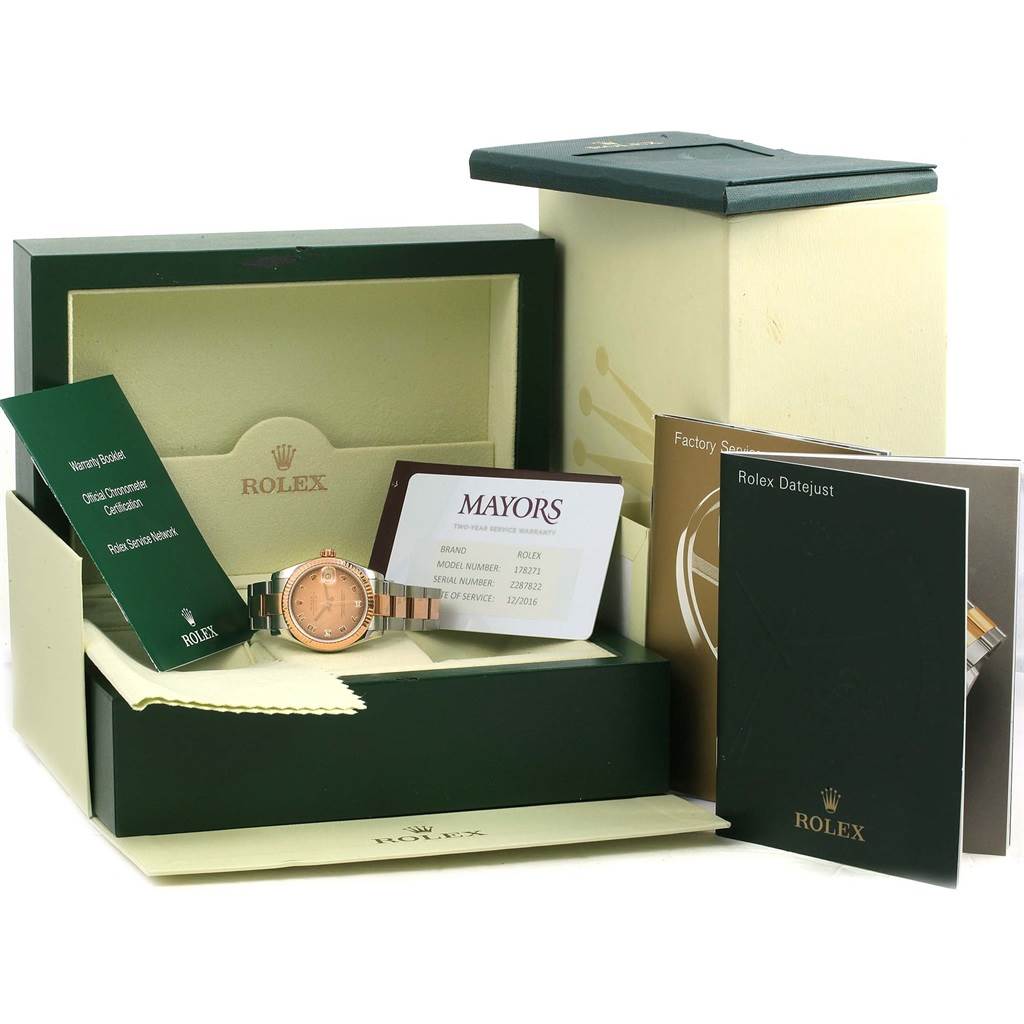 The image shows a Mid-Size Rolex watch in its box, accompanied by documentation and accessories from a frontal angle.