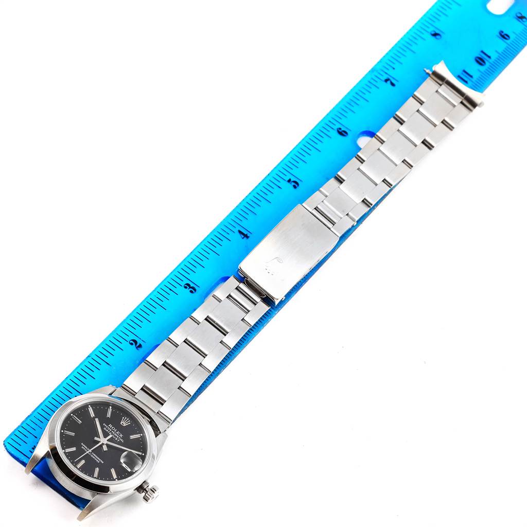 The Rolex Mid-Size 68240 Women's Stainless Steel Black Dial 68240 Women's Stainless Steel Black Dial model watch is shown in a top view, including the face, bezel, bracelet, and clasp positioned next to a ruler.