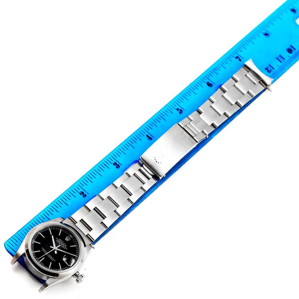 This image shows a top-down view of a Rolex Mid-Size 78240 Women's Stainless Steel Black Dial 78240 Women's Stainless Steel Black Dial watch with a metal bracelet next to a blue ruler.